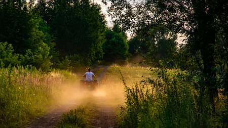 young man driving a quad bike down a dirt road at sunset