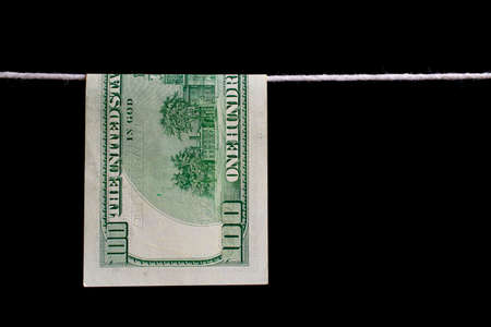 one hundred US dollar banknote hanging on a cord on a black background