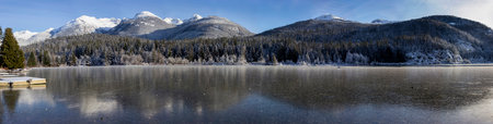 Stunning winter landscape panorama. Frozen lake and snow capped mountains reflecting back on iceの写真素材