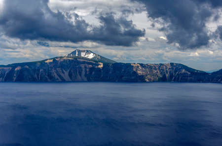 Beautiful scenery at Crater lake. Snowy mountain range around the rim. Cloudy, blue sky. Deep, dark blue lake.の写真素材