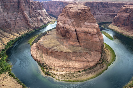 Captured on a serene afternoon, the Colorado River gracefully curves around the dramatic rock formations of Horseshoe Bend in Arizona, showcasing nature's stunning beauty.の写真素材