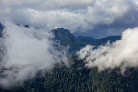 Dramatic clouds roll over a mountain range, shrouding peaks and valleys in mist. This natural...