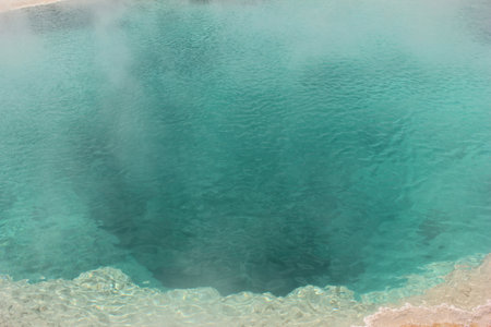 Bright turquoise water fills a geothermal spring, with steam rising into the air, creating a serene and mystical atmosphere. The natural beauty showcases vibrant colors and unique landscapes.の写真素材
