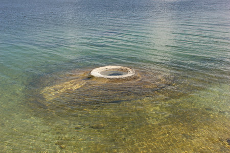 Calm water reflects sunlight as a circular stone structure emerges from the lake floor. Gentle ripples extend outward, creating a serene atmosphere in a natural environment.の写真素材