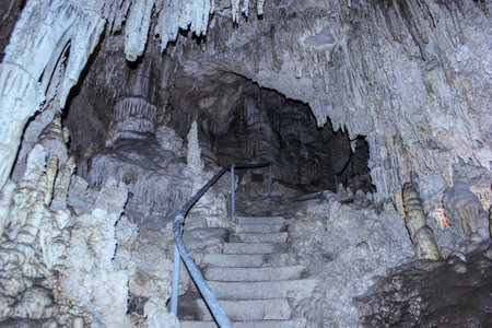 A winding staircase leads into a vast underground cave adorned with impressive stalactites and stalagmites. The eerie atmosphere creates a sense of adventure and discovery.の写真素材