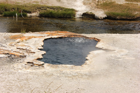 This location features a bubbling hot spring surrounded by unique geological formations. The vivid orange hues contrast against the clear blue water, highlighting nature's dynamic processes.の写真素材