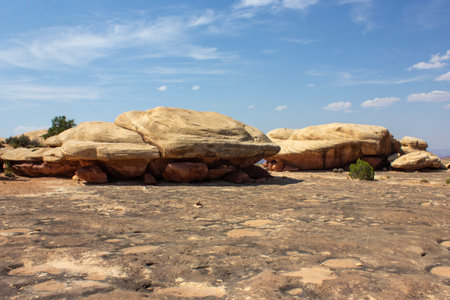 Massive sandstone rocks rise from the ground, surrounded by a dry rocky terrain under an expansive blue sky. The scene highlights the unique geological formations in this tranquil desert area.の写真素材