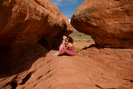 A woman relaxes in a serene location, nestled between two towering rock formations in a vibrant desert. She is holding her baby.の写真素材