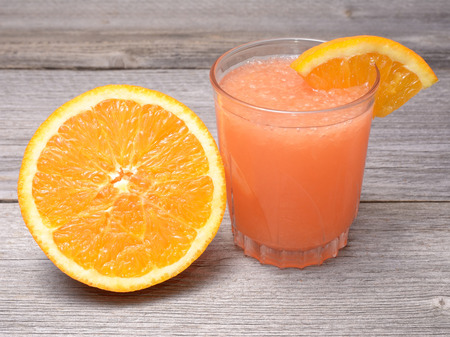 Glass of orange juice with sliced orange half on wooden tableの写真素材