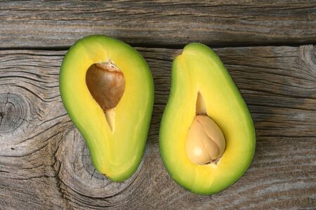 avocados one cut in two with seed, on wooden surfaceの写真素材