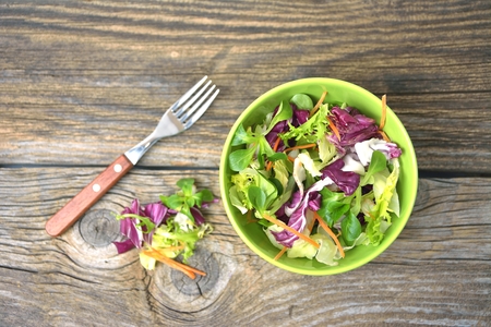 Fresh mixed green salad in bowl on wooden table close upの写真素材