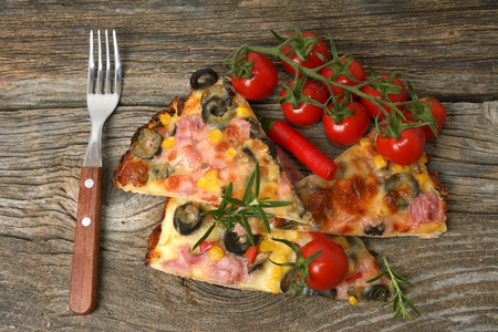 sliced ham pizza with capsicum and olives on wooden board on tableの写真素材