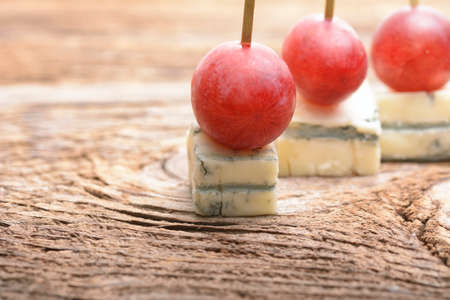 pieces of blue cheese and red grapes isolated on a wooden tableの写真素材