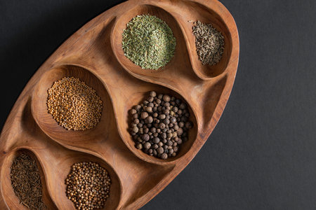 Various colorful herbs and spices on wooden table, isolated on black background. mustard, rosemary, cumin, coriander, anise, allspice on a board.の写真素材