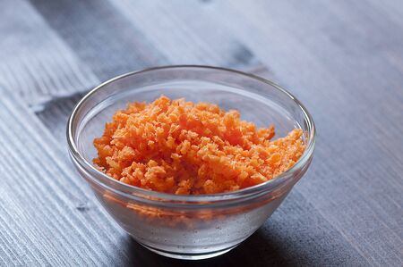 Minced carrots in a glass bowl on a wood backgroundの写真素材