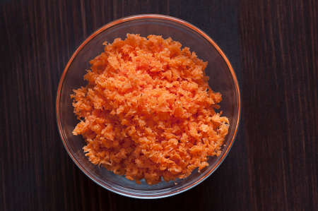 Minced carrots in a glass bowl on a wood backgroundの写真素材