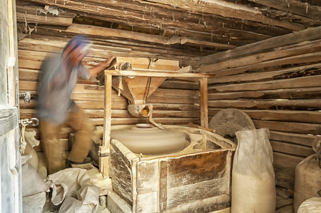 Man working in a small mill. Man making corn flour. Wooden water mill interior. Long exposure.の写真素材