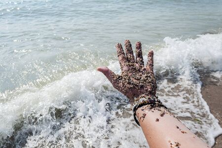 Hand covered with beach sand. Sea and foam in the background.の写真素材