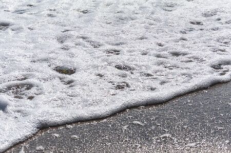 Wave with foam on a sandy beachの写真素材