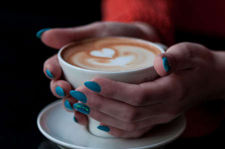 Close-up of hands holding a coffee cup with heart shape. Focus on hands.の写真素材