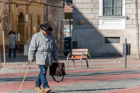 TIMISOARA, ROMANIA - MARCH 15, 2018: Man with a bag and a walking stick. Walking on the street, in the city. Real people.のeditorial素材