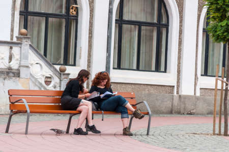 TIMISOARA, ROMANIA - SEPTEMBER 13, 2016: Two girls sitting on a bench. Real people.のeditorial素材