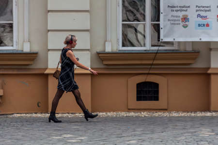 TIMISOARA, ROMANIA - SEPTEMBER 13, 2016: Woman walking on the street and listening music on her phone. Real people.のeditorial素材