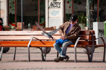 Timisoara, Romania - April 13, 2016: Man sitting on a bench and smoking a cigarette on the street. Real people.のeditorial素材