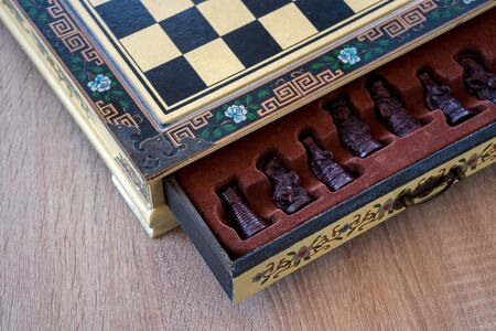 Close-up of a chess table. Beautiful box with floral decorations. Opened drawer with chess pieces