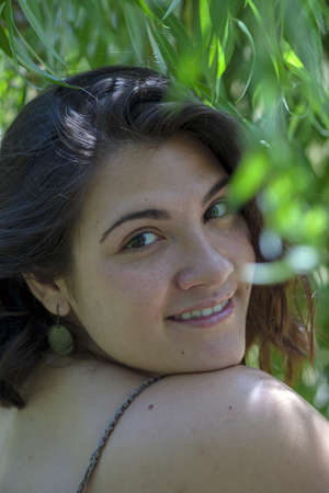 Portrait of a woman under a willow tree with green leaves