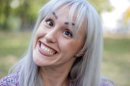 Outdoors portrait of a woman making funny faces. Silver hair.