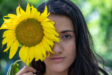Portrait of a woman holding a sunflower over her faceの写真素材