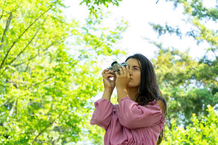 Woman in a pink dress taking photographs with a vintage film camera in a park