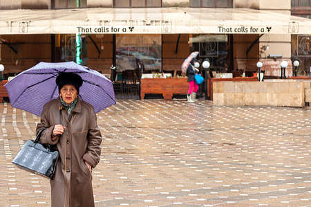 Timisoara, Romania - March 23, 2016: Woman walking on the street in the rain with an umbrella in hand. Motion blur. Real people.のeditorial素材