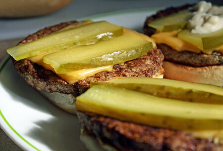 Barbecued Cheeseburgers just of the grill with sliced dill pickles on a toasted bunの写真素材