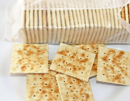 Crispy soda crackers on plate. Open package in backgroundの写真素材