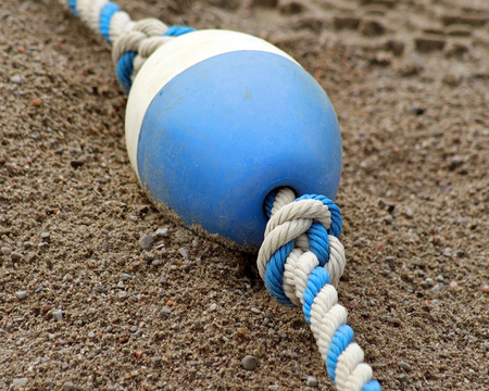 Blue and white plastic BUOY laying on sand at beachの写真素材