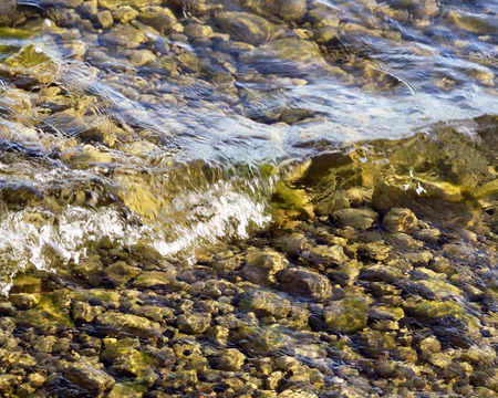 Small waves of crystal clear lake waters moving over rock bottom