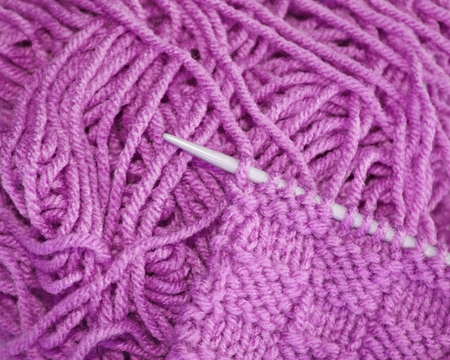 Knitted stitches on knitting needle with strands of lilac colored yarn in background