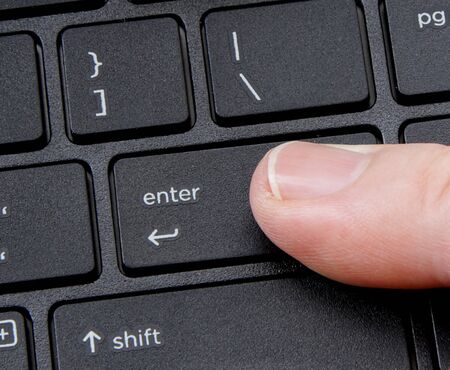 computer enter key with finger pressing button on white backgroundの写真素材