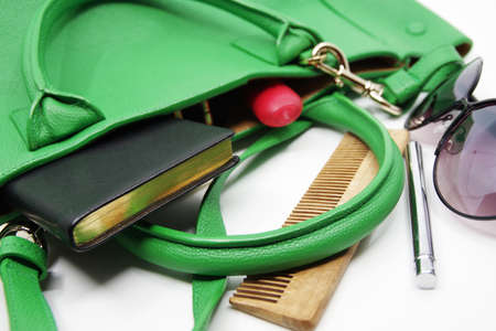 Things from lady purse isolated on white background. Cosmetics and women's accessories fell out of green handbag. Notebook, wooden comb, lipstick, sunglassesの写真素材