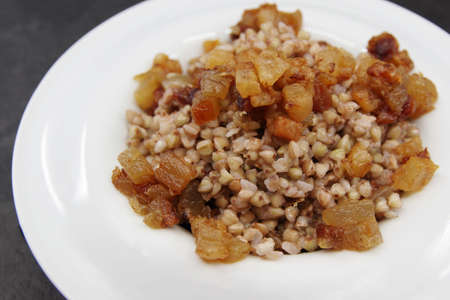 Buckwheat porridge with pork cracklings served in a plate. Black background. Closeup