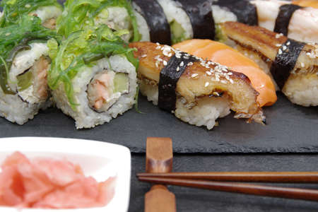 Japanese sushi food on a black tray, served with ginger, soy sauce and seaweed salad. Sushi rolls, salmon nigiri, shrimp nigiri, unagi nigiriの写真素材