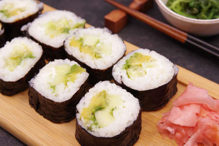 Japanese Maki rolls with cucumber and avocado on a wooden tray, served with ginger, soy sauce and seaweed salad.の写真素材