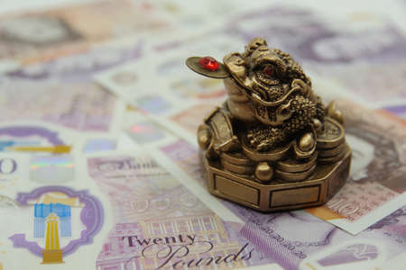 Chinese Feng Shui lucky money frog sitting on 10 and 20 UK pounds banknotes. Closeupの写真素材