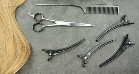 Blonde curl of hair and hairdresser set isolated on gray background - scissor and combs. Beauty concept.の写真素材