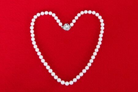 Pearl necklace in the shape of a heart on red backgroundの写真素材