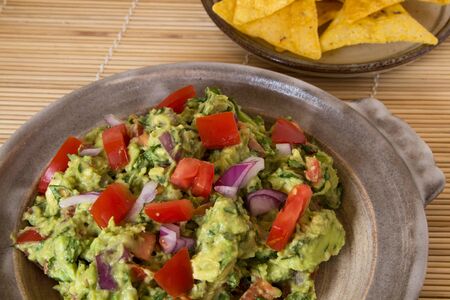 Guacamole and corn chips served in a pottery dish on a bamboo matの写真素材