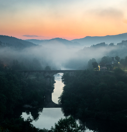 Mist is formed along a river valley during a sunrise with a bridge in the foreground.の写真素材
