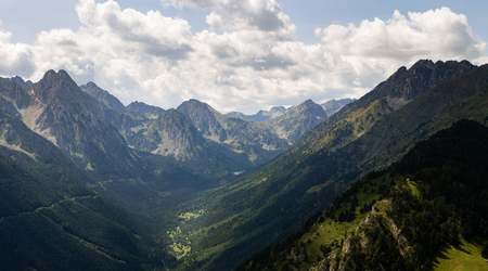Panorama of a mountain valley with various trees along the hillsides and distant peaks in the horizon.の写真素材